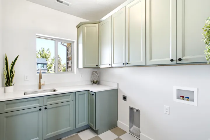 White shaker-style upper cabinetry, contrasting sage lower cabinetry, white solid surface countertops, stainless steel undermount sink, and a gold-tone faucet