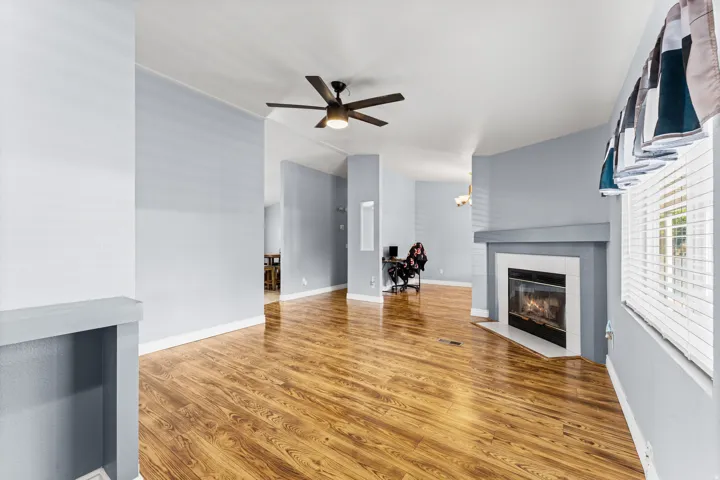 Wood-finish flooring throughout, ceiling fan with integrated lighting, built-in fireplace, and window with blinds