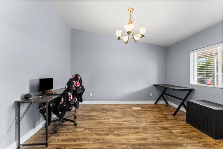 Wood-finish flooring, vaulted ceiling, multi-light chandelier, and a window with blinds
