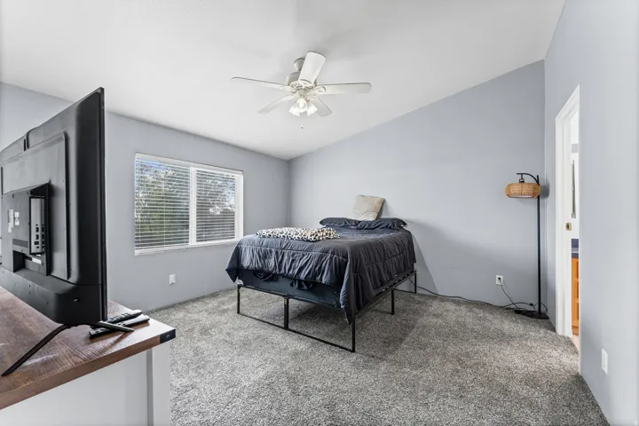 Vaulted ceiling, ceiling fan, window with blinds, light gray carpet, and wood-finish countertop