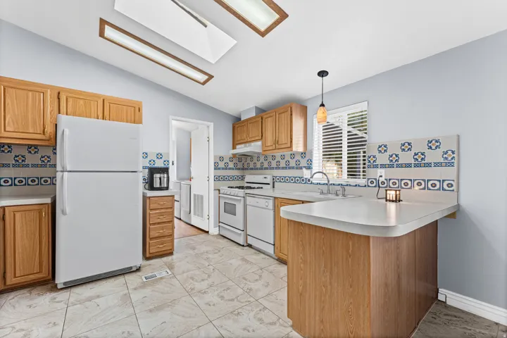 Kitchen featuring a breakfast bar, white appliances, wood cabinetry, patterned tile backsplash, and skylights