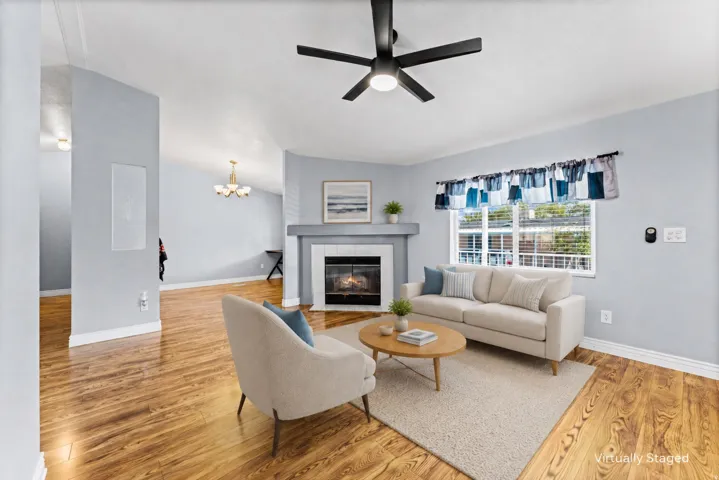 Vaulted ceiling living area featuring wood-finish flooring, a contemporary ceiling fan, and a fireplace with a mantel