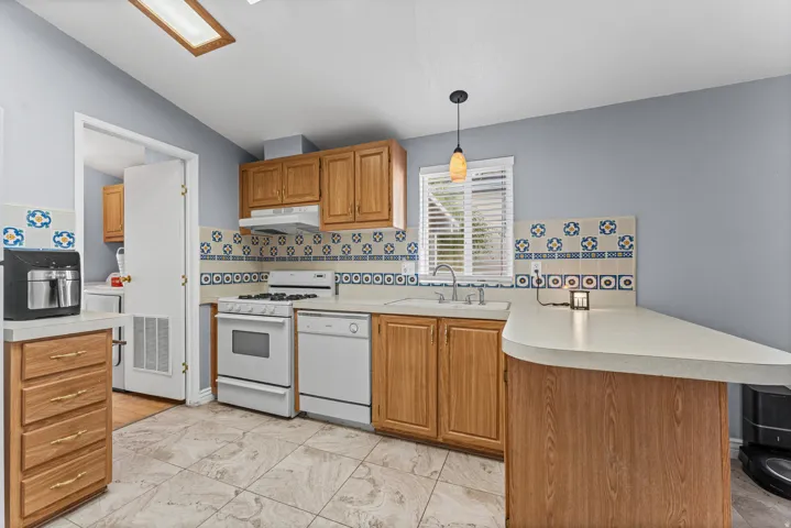 Kitchen featuring wood cabinetry, tile flooring, counter seating, white appliances, and a decorative tile backsplash