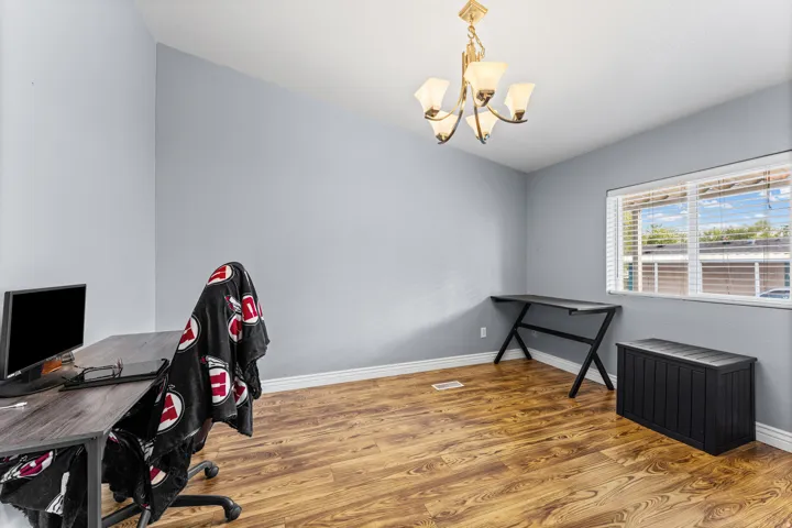 Vaulted ceiling, wood-finish flooring, single window with blinds, and an overhead chandelier light fixture