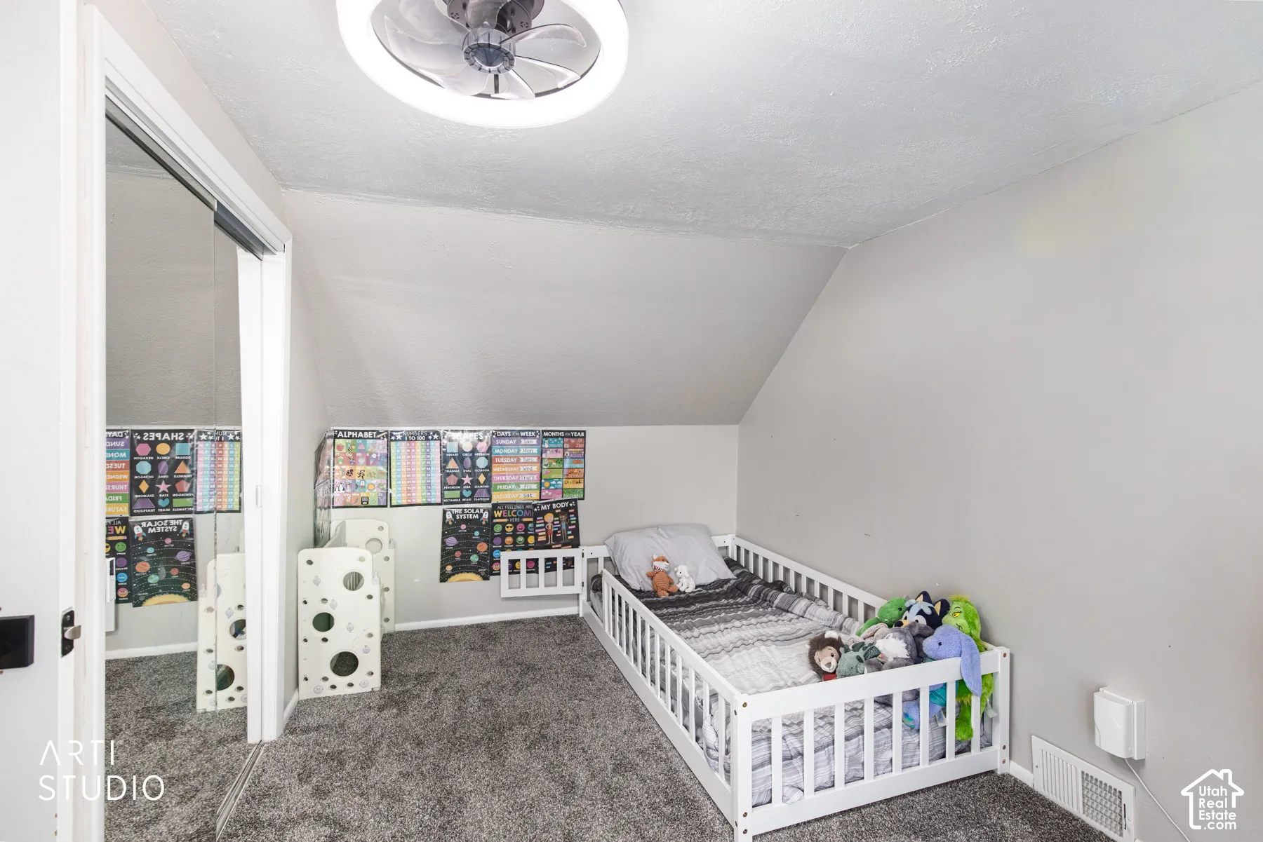 Sloped ceiling room featuring a ceiling-mounted fan with integrated lighting, carpeted flooring, and a mirrored closet door