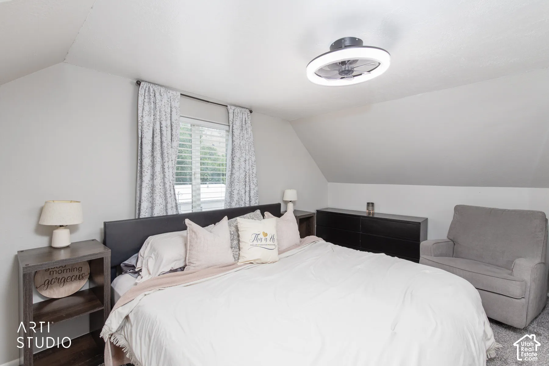 Sloped ceiling architecture with a window featuring louvered shutters and drapes, a flush-mount ceiling light with a fan, and wall-to-wall carpeting