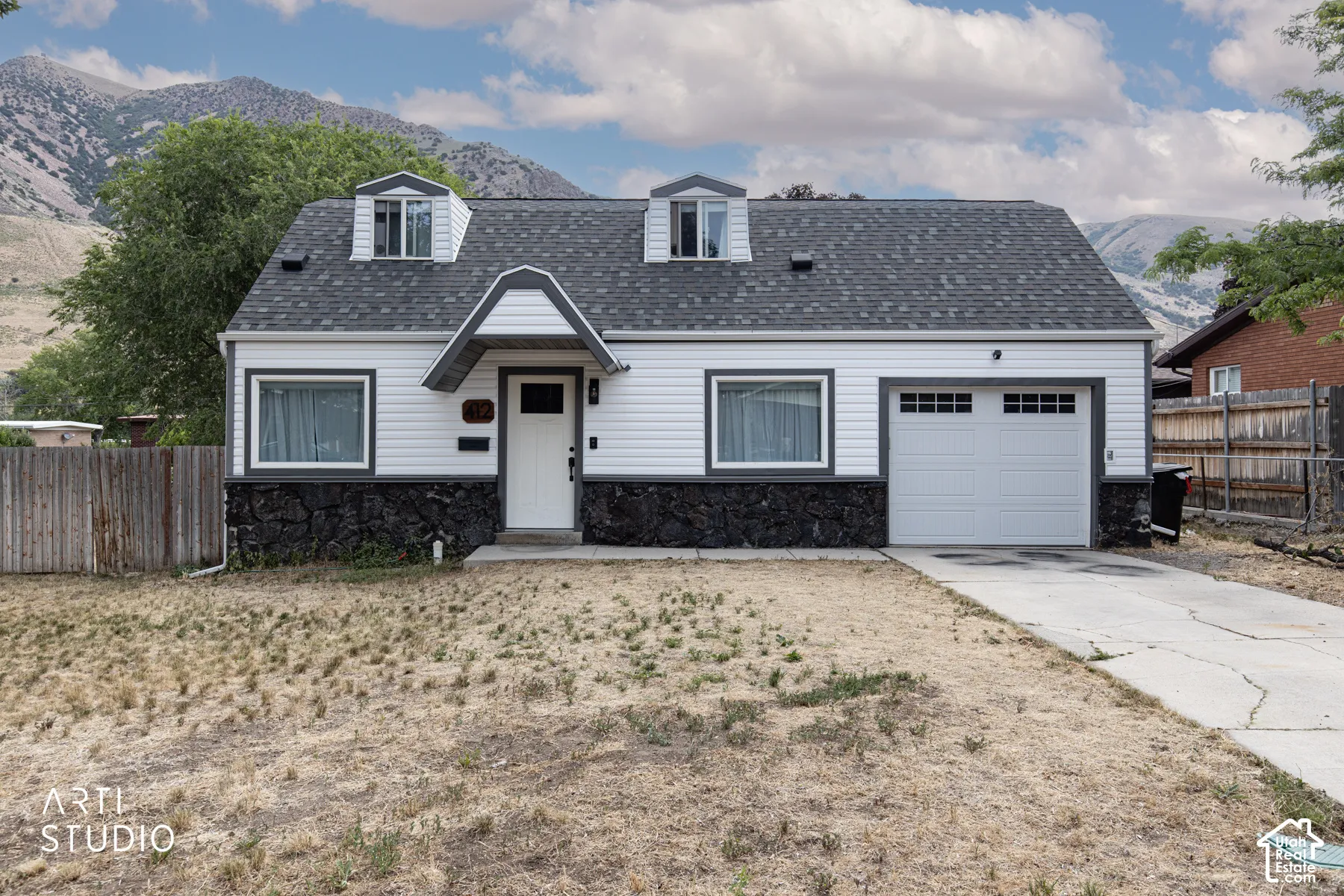 White siding exterior with dark grey trim, a dark asphalt shingle roof, three dormer windows, and a single-car garage