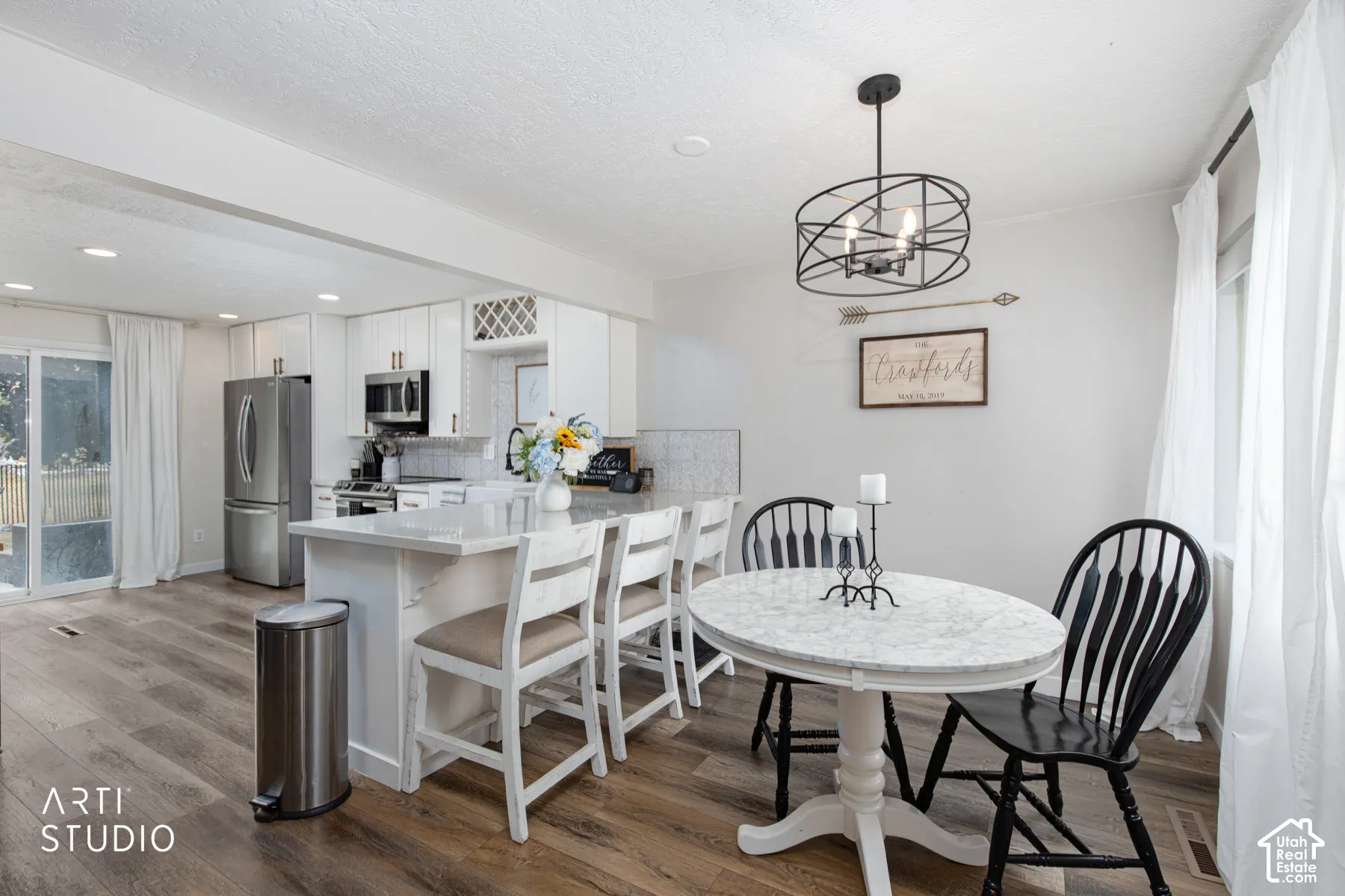 Open-concept kitchen and dining area featuring stainless steel refrigerator and built-in appliances, white cabinetry with quartz countertops, a central island with seating for multiple guests, wood-finish flooring throughout, and a round pedestal dining t