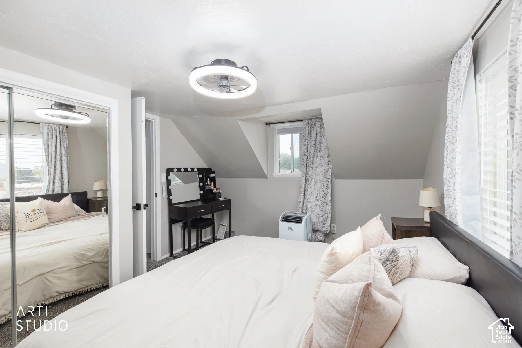 Sliding mirrored closet doors, contemporary ceiling fan, window with blinds and curtains, and sloped ceiling details