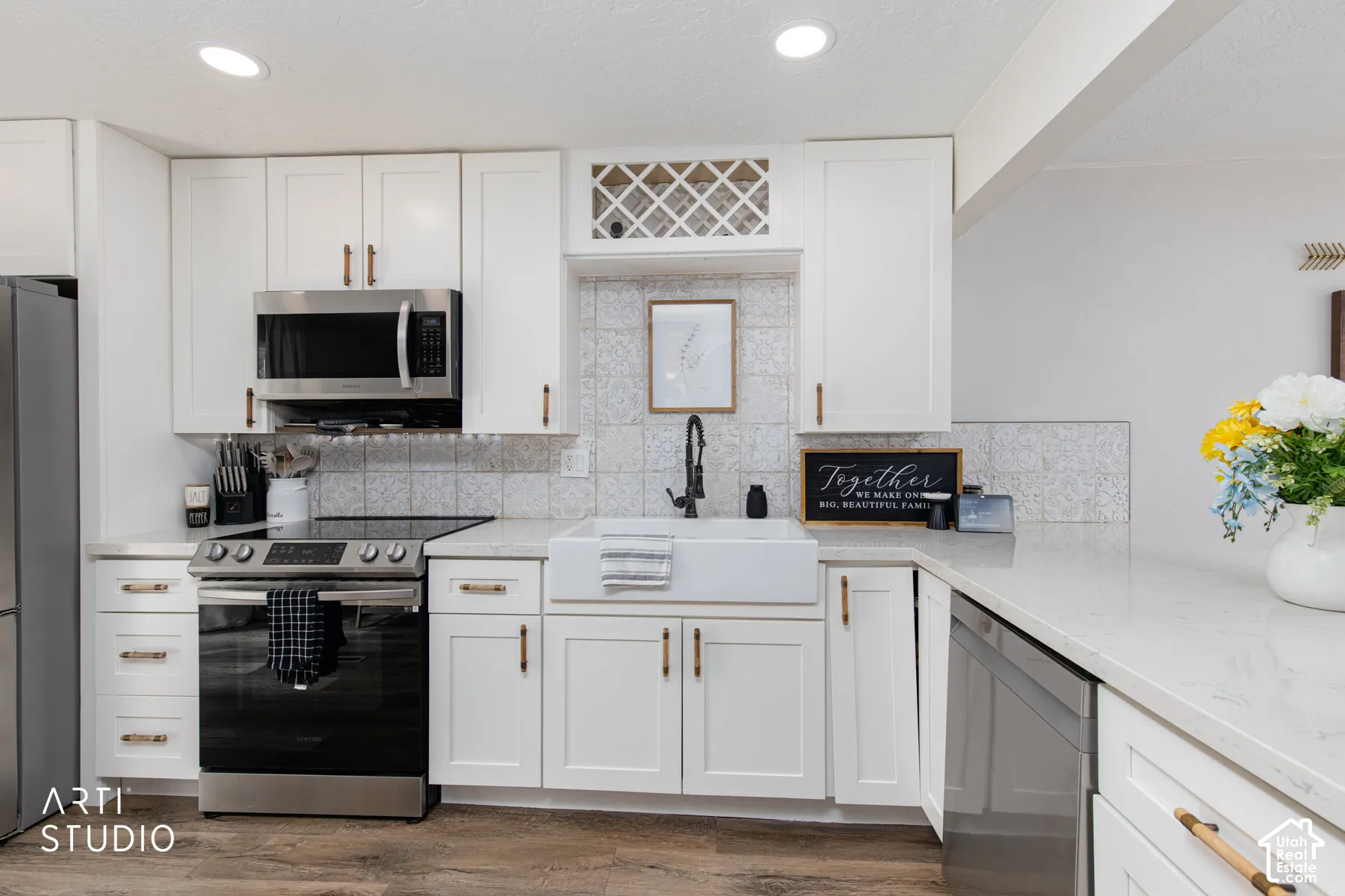 Contemporary kitchen featuring white shaker-style cabinetry with brushed gold hardware, stainless steel gas range and microwave, quartz countertops, subway tile backsplash, and wood-finish flooring throughout the space