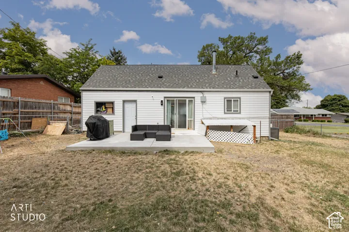 White vinyl siding exterior with a gray shingle roof, concrete patio, and a sliding glass door