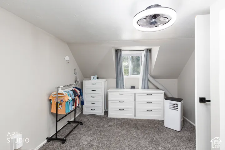 Recessed window with gray drapery, sloped ceiling, and textured carpet flooring