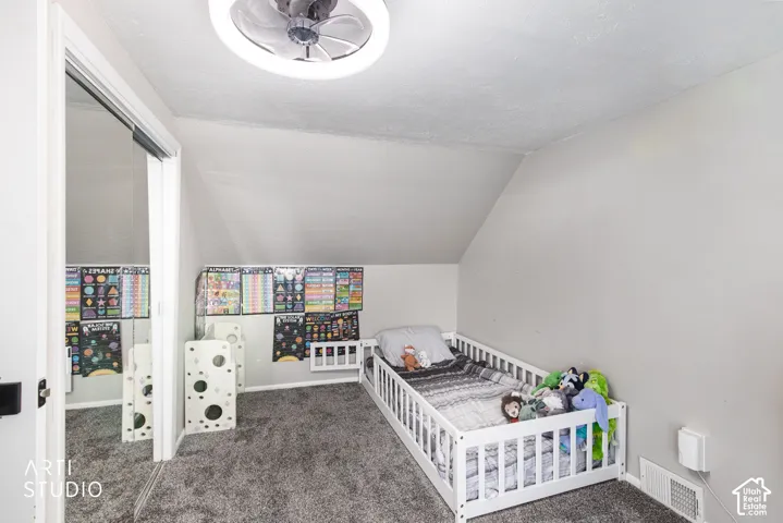 Sloped ceiling room featuring a ceiling-mounted fan with integrated lighting, carpeted flooring, and a mirrored closet door