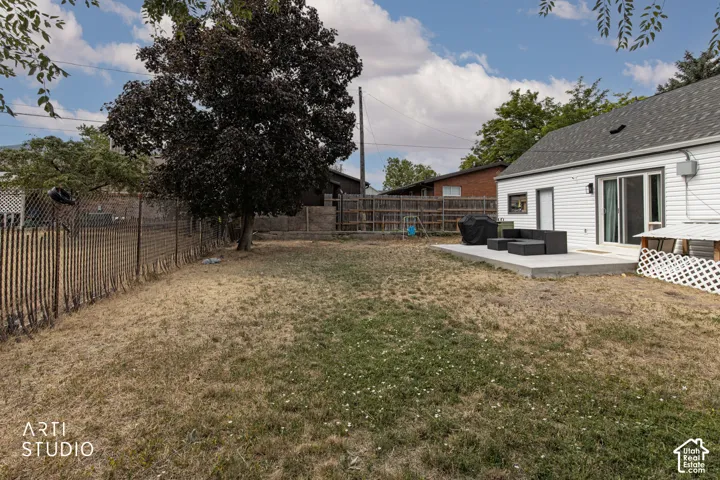 Expansive backyard featuring a mature tree, concrete patio, and white siding exterior with sliding glass doors