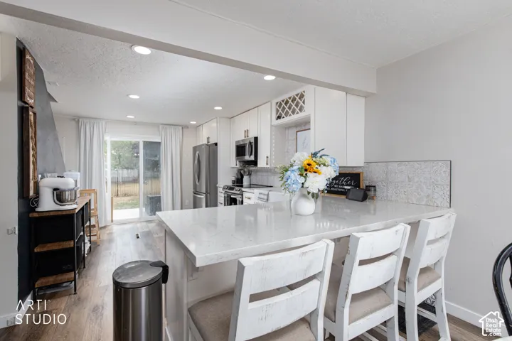 Modern kitchen featuring white cabinetry, stainless steel appliances, a quartz waterfall island with seating for three, subway tile backsplash, recessed lighting, and direct access to the backyard through sliding glass doors