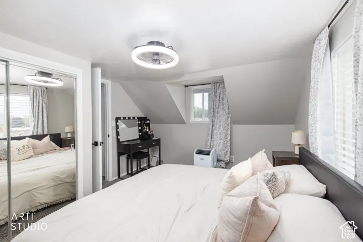 Sliding mirrored closet doors, contemporary ceiling fan, window with blinds and curtains, and sloped ceiling details