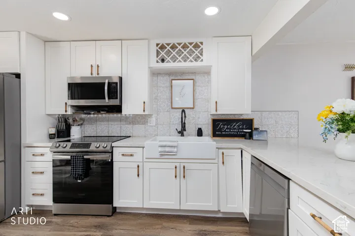 Contemporary kitchen featuring white shaker-style cabinetry with brushed gold hardware, stainless steel gas range and microwave, quartz countertops, subway tile backsplash, and wood-finish flooring throughout the space
