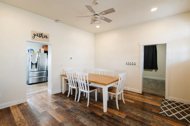 Dining area featuring hardwood flooring, a wood-top dining table with white chairs, ceiling fan with integrated lighting, stainless steel refrigerator with French doors, and neutral wall finishes throughout the open-concept space