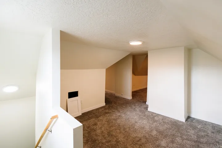 Carpeted loft area with sloped ceilings, recessed lighting, and a wood handrail