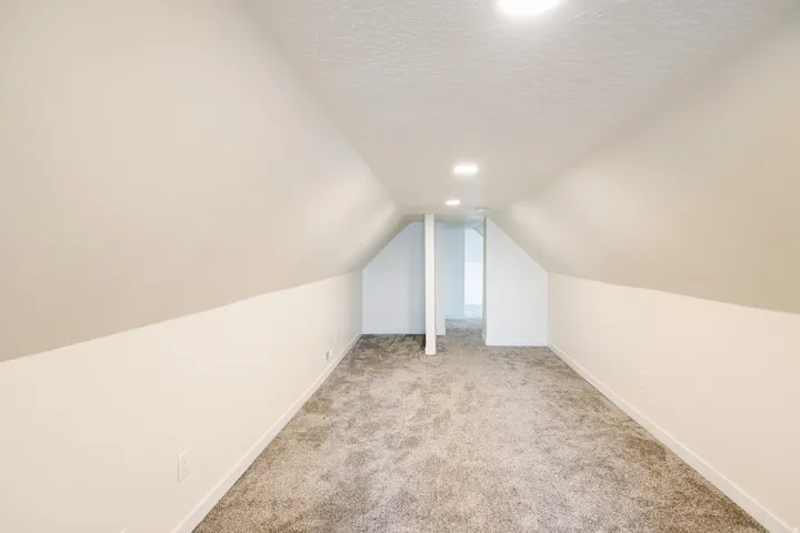 Spacious room with sloped ceilings, recessed lighting, neutral-toned walls, and grey carpet flooring