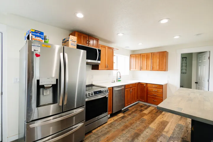Kitchen featuring wood-finish flooring, stainless steel appliances, wood cabinetry, light countertops, and recessed lighting