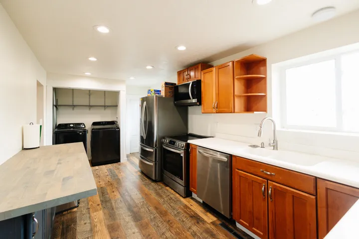 Wood-finish flooring, recessed lighting, and a kitchen featuring a stainless steel dishwasher, stainless steel refrigerator, and wood cabinetry