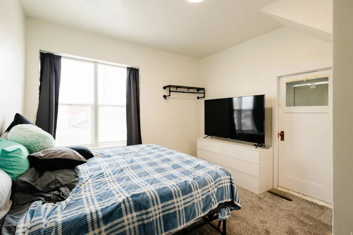 White interior paint, light-colored carpeting, large window with dark drapes, white paneled door with glass insert