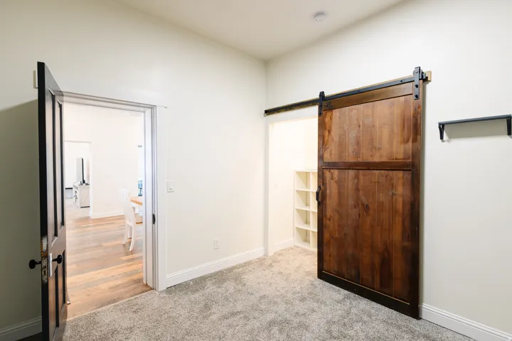 Textured carpet flooring, custom wood barn door with black hardware, built-in shelving, and a solid core interior door