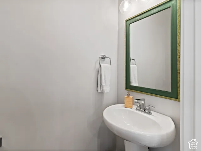 Powder room featuring a curved pedestal sink with chrome faucet, green-framed mirror, and bright overhead lighting