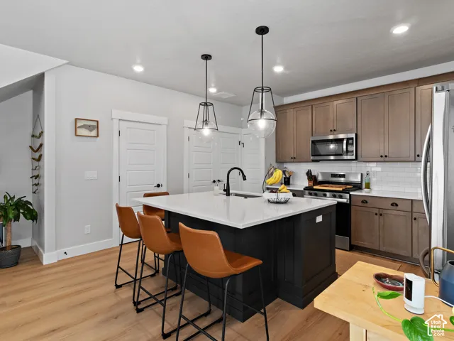 Spacious kitchen featuring a central island with a white countertop, two pendant lights, wood-finish flooring, and stainless steel appliances