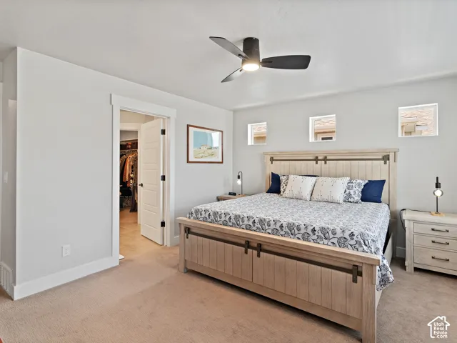 Spacious primary bedroom with wood-finish bed frame featuring metal hardware accents, neutral carpet flooring, and abundant natural light from multiple windows
