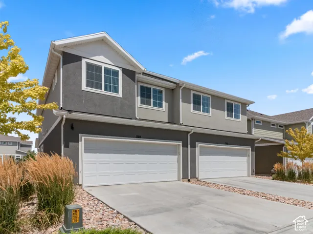 Stucco exterior with white trim, two-car garage, concrete driveway, and rock landscaping