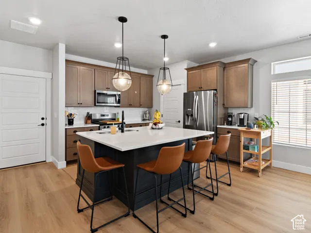Kitchen featuring a center island with countertop seating, stainless steel appliances, wood-finish flooring, and pendant lighting