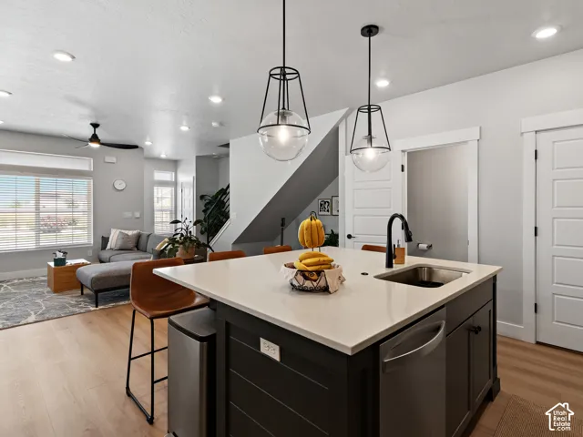 Kitchen island with a light-toned countertop, built-in sink with a black faucet, recessed lighting, and wood-finish flooring