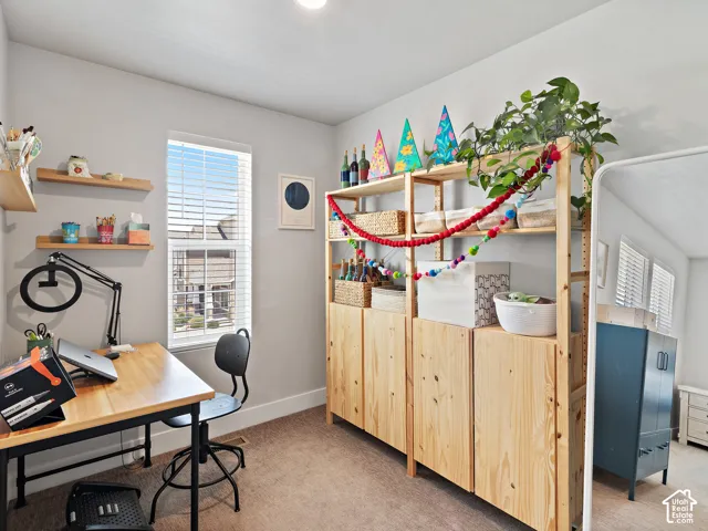 Master bedroom includes a bright home office  area featuring natural light from a large window, wood-finish shelving with built-in storage cabinetry, carpet flooring, and a sturdy work desk with task lighting