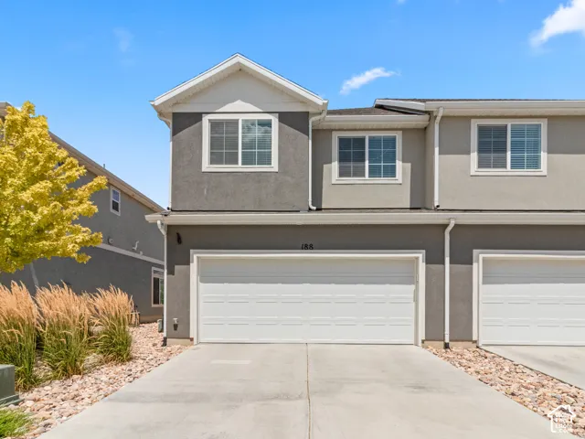 Multi-story exterior with stucco siding, white-framed windows, an attached garage, and a concrete driveway with decorative stone accents