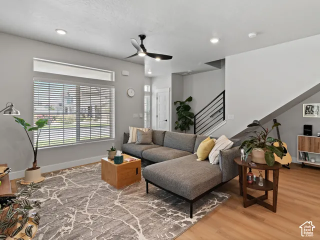 Recessed lighting, wood-finish flooring, staircase with metal railing, ceiling fan, and large window with blinds