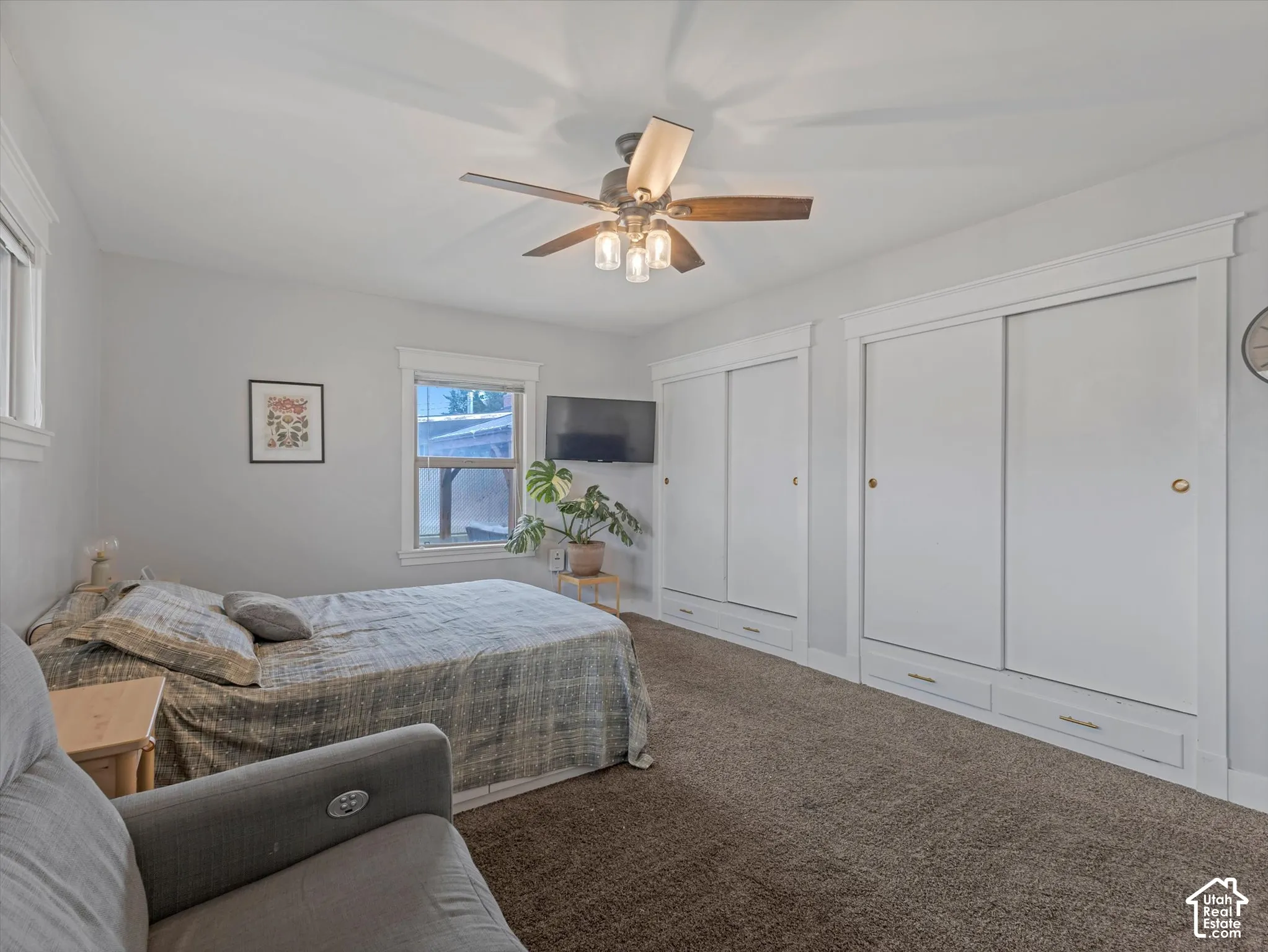 Carpeted room with ceiling fan, two windows with white trim, and two built-in sliding door closets with integrated drawers