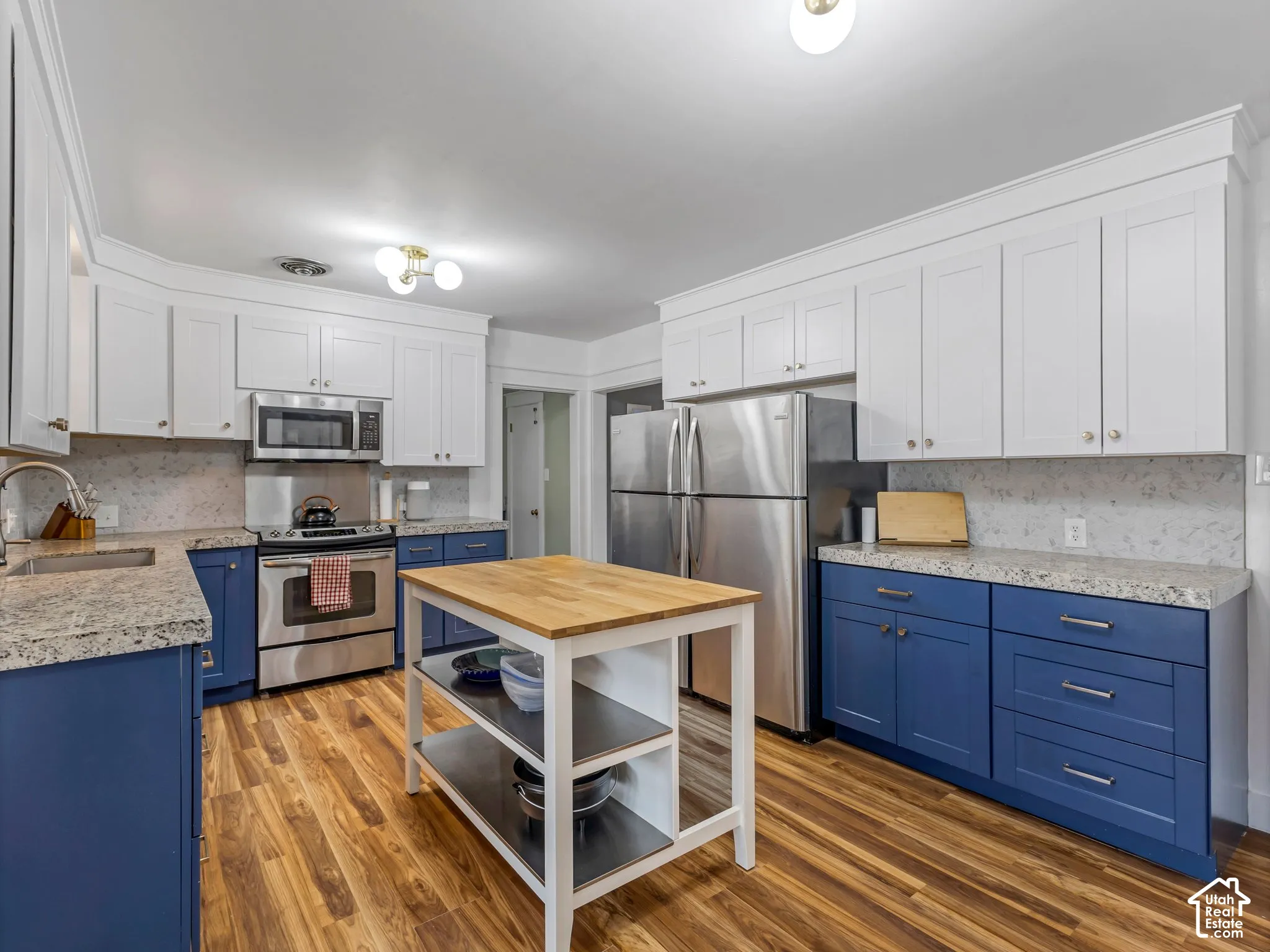 Kitchen featuring LVP flooring, blue and white cabinetry, stone countertops, stainless steel appliances, and a central island with a wood-finish top