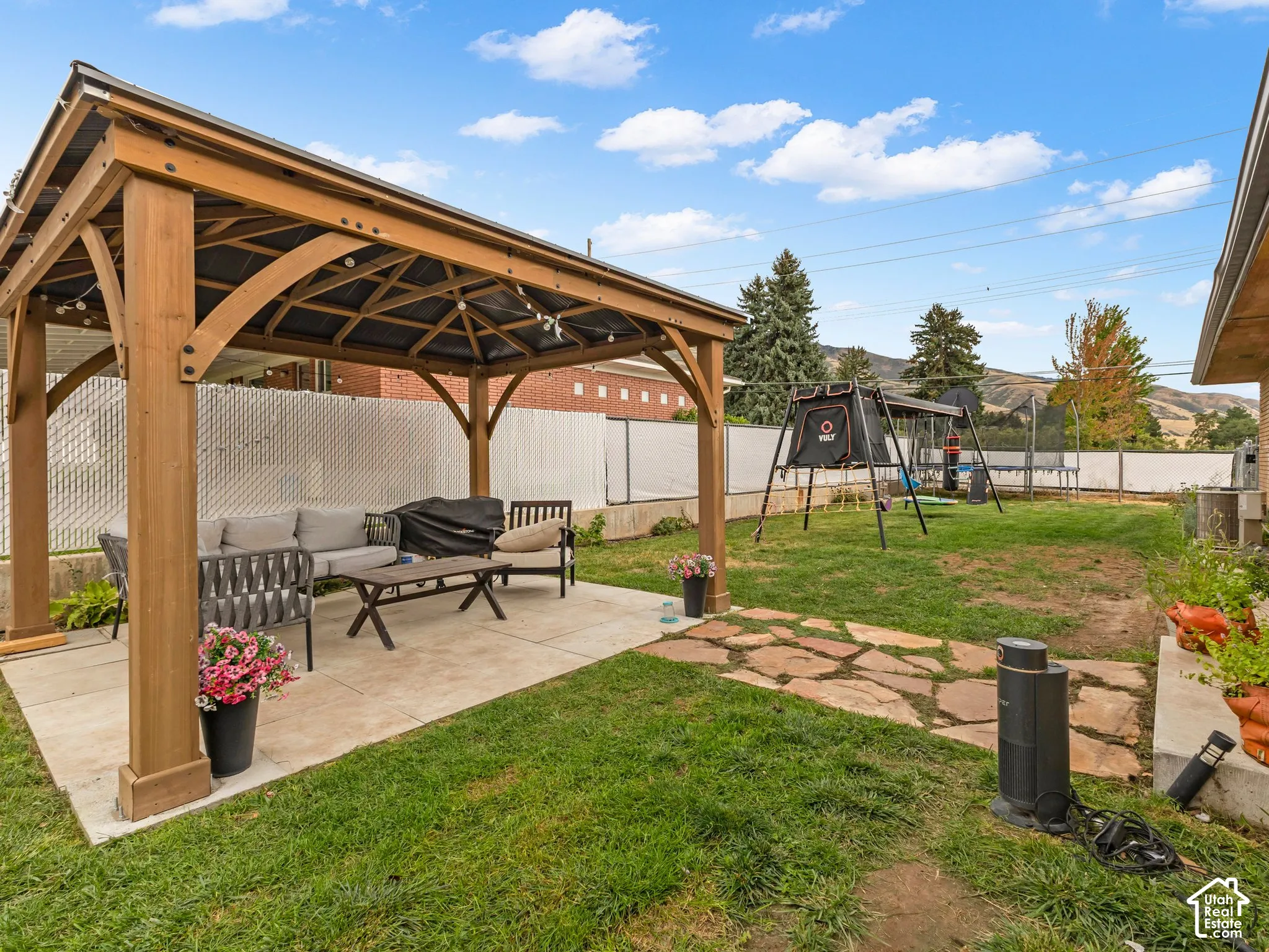 Expansive backyard featuring a wood-frame gazebo, concrete patio, stone pathway, and mature trees