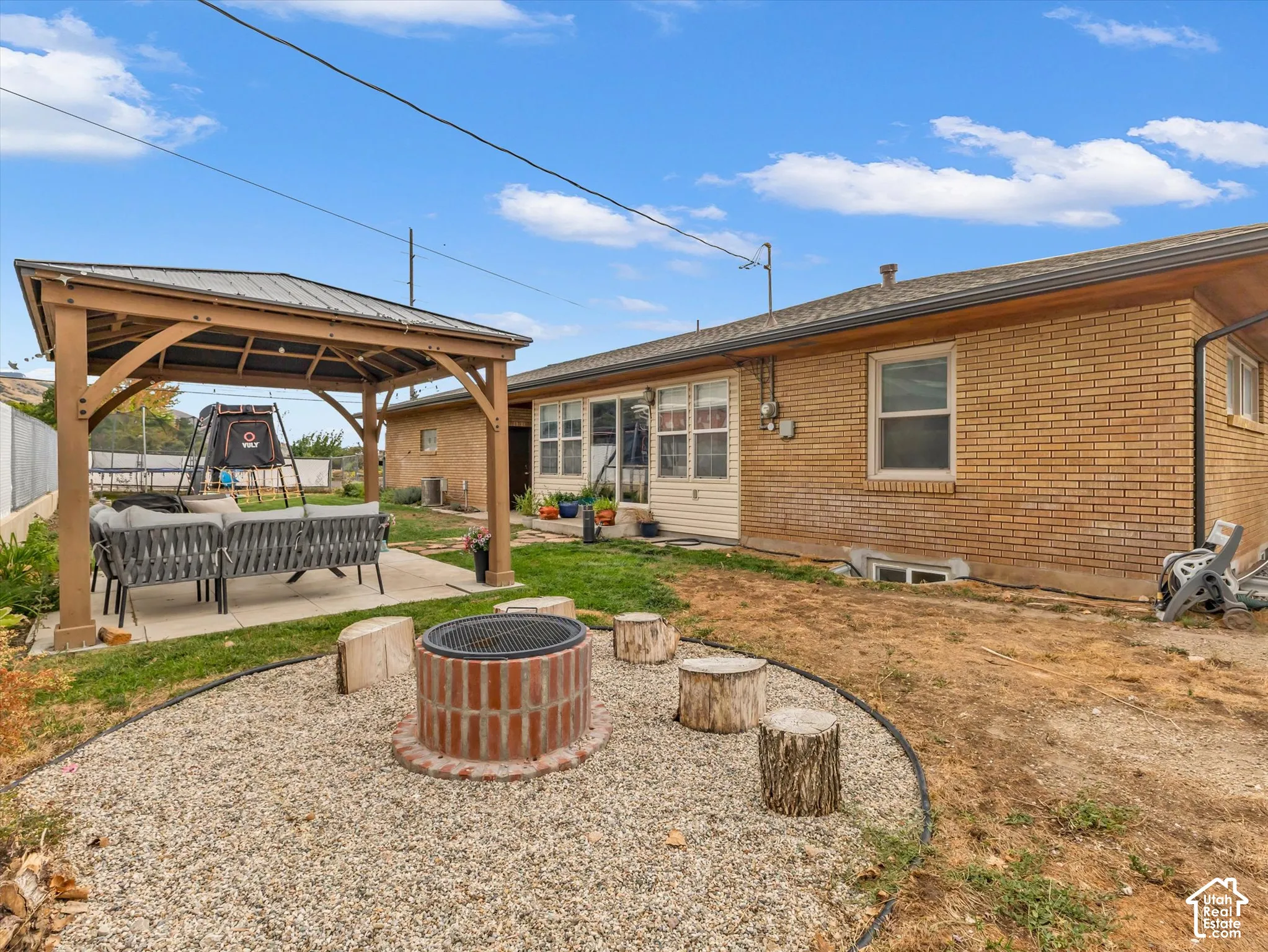 Expansive backyard featuring a wood-frame gazebo with a metal roof, a brick fire pit with gravel surround, and a brick exterior building with multiple windows