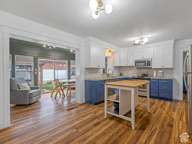 Two-tone kitchen cabinetry, wood-finish flooring, stainless steel appliances, granite-style countertops, and a kitchen island with a butcher block top