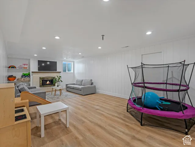 Recessed lighting, wood-finish flooring, white paneled walls, built-in shelving, and a fireplace with a stone surround