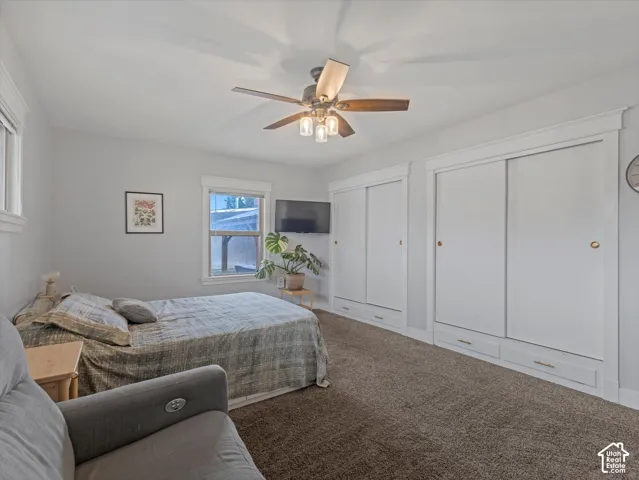 Carpeted room with ceiling fan, two windows with white trim, and two built-in sliding door closets with integrated drawers