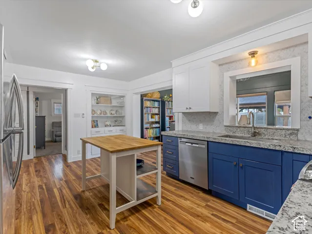 Kitchen featuring wood-finish flooring, blue lower cabinetry, white upper cabinetry, light-toned countertops, and a stainless steel dishwasher