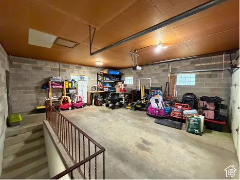 Spacious garage with concrete block walls, concrete flooring, and an integrated staircase with metal railing