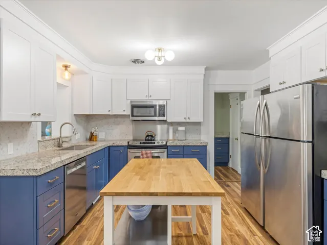 Kitchen featuring two-tone cabinetry, light-toned countertops, wood-finish flooring, a stainless steel sink, and a center island with a wood-finish top