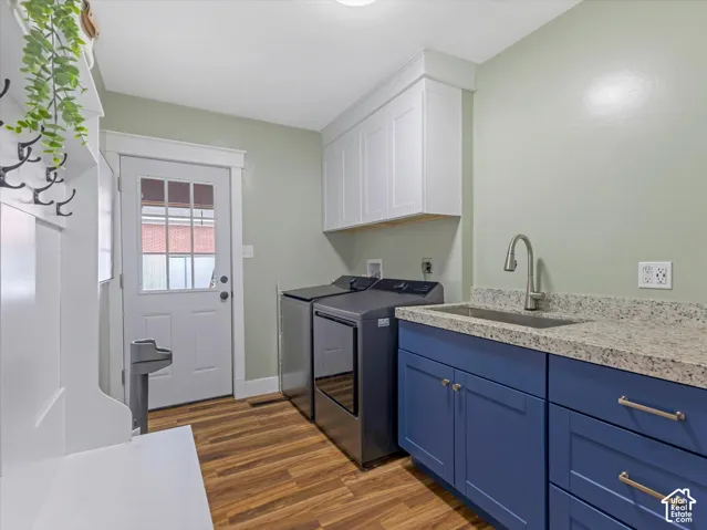 Laundry area featuring wood-finish flooring, built-in white cabinetry, blue base cabinetry with a stainless steel sink, and light-toned countertop