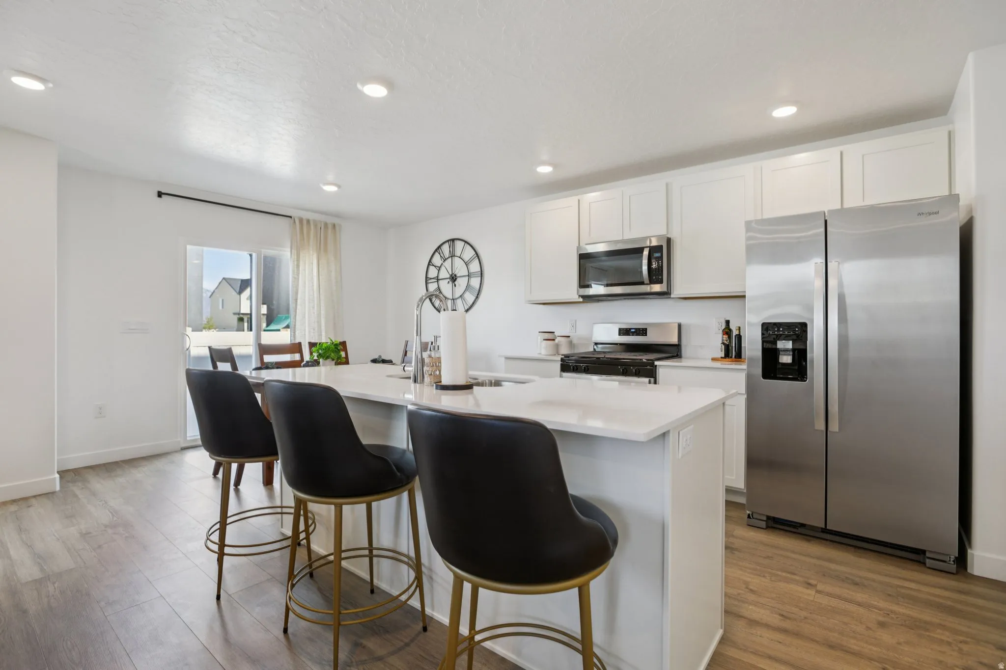 Kitchen featuring white cabinetry, stainless steel appliances, a center island with countertop seating, and wood-finish flooring