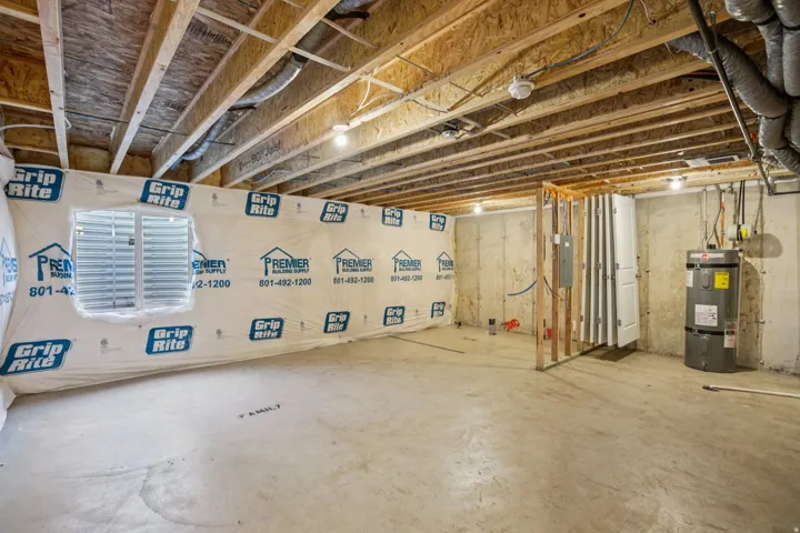 Unfinished basement with exposed ceiling joists, concrete flooring, a window, and a water heater